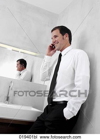 portrait of young businessman in front of mirror in bathroom talking on mobile phone View Large Photo Image Stock Image - portrait of young businessman in front of mirror in bathroom talking on mobile phone. Fotosearch