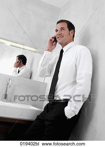 portrait of young businessman in front of mirror in bathroom talking on mobile phone View Large Photo Image Stock Image - portrait of young businessman in front of mirror in bathroom talking on mobile phone. Fotosearch
