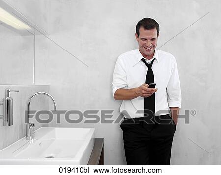 portrait of young businessman in front of mirror in bathroom looking at mobile phone View Large Photo Image Stock Image - portrait of young businessman in front of mirror in bathroom looking at mobile phone. Fotosearch
