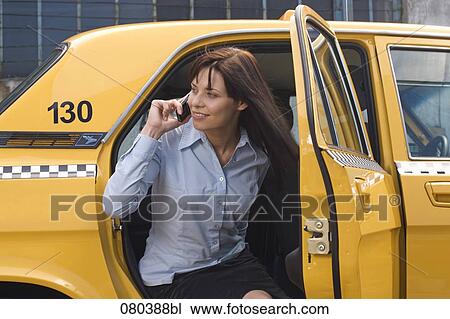 Stock Image - portrait of young businesswoman leaving yellow taxi talking on mobile phone. Fotosearch