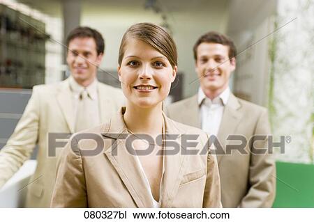 Stock Image - portrait of young businesswoman with two male colleagues in the background. Fotosearch