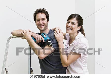 Stock Image - portrait of young couple in new home man holding cordless screwdriver. Fotosearch