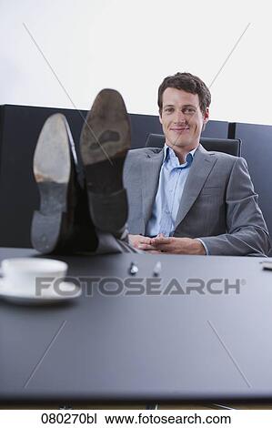 Stock Image - portrait of young entrepreneur sitting with his feet on desk . Fotosearch