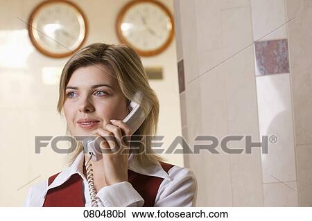 Stock Image - portrait of young hotel receptionist talking on telephone. Fotosearch