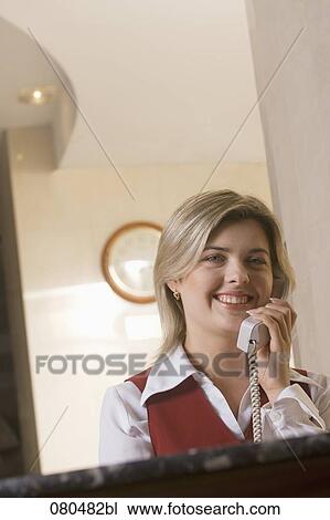Stock Image - portrait of young hotel receptionist talking on telephone. Fotosearch