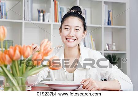 Stock Image - portrait of young japanese girl eating at table. Fotosearch