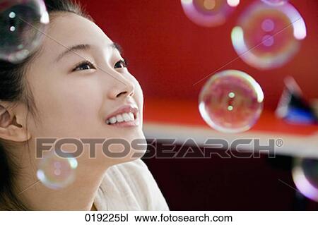 Stock Image - portrait of young japanese girl playing with soap bubbles. Fotosearch