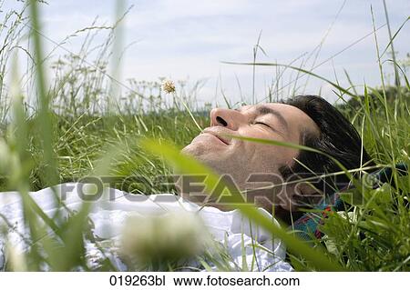 Stock Image - portrait of young man dozing in grass. Fotosearch