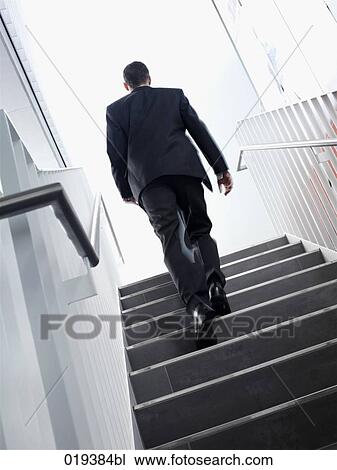Stock Image - rear view of young businessman walking up stairs. Fotosearch
