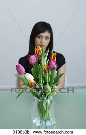 Stock Image - sad looking asian woman sitting behind flower vase. Fotosearch