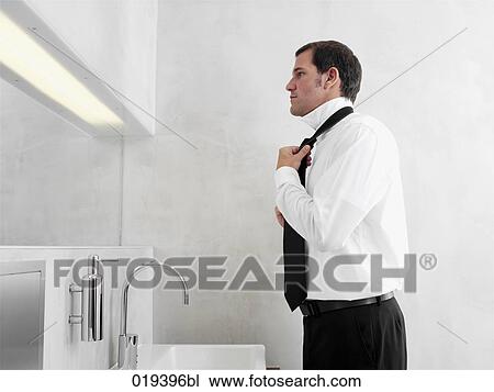 Stock Image - side view of businessman putting on his tie. Fotosearch
