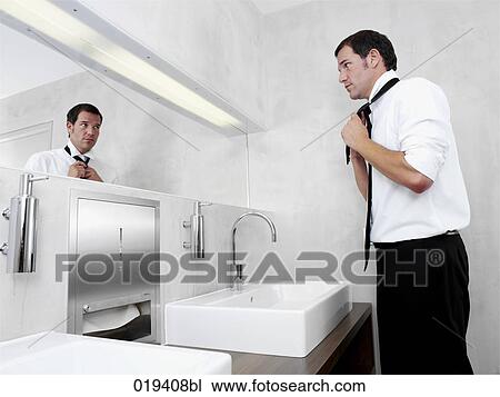 Stock Image - side view of businessman putting on his tie in public restroom. Fotosearch