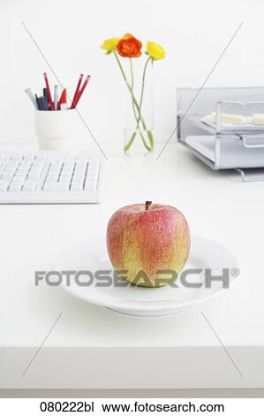 Stock Image - still life of red apple on plate on office desk. Fotosearch