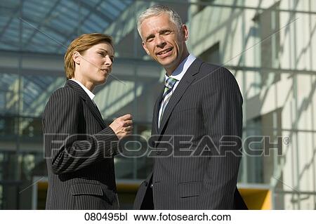 Stock Image - two mature business people having conversation in front of office building. Fotosearch
