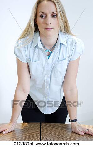 Stock Image - wistful looking blonde office worker leaning on table. Fotosearch