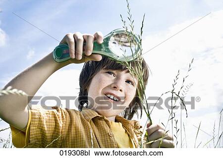 Stock Image - young boy looking at grass through magnifying glass. Fotosearch