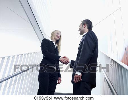 Stock Image - young businesswoman and man shaking hands in office building. Fotosearch