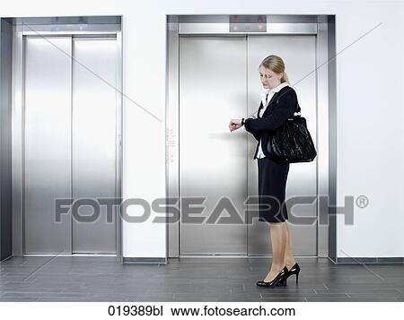 Stock Image - young businesswoman standing in front of elevator looking at her watch. Fotosearch