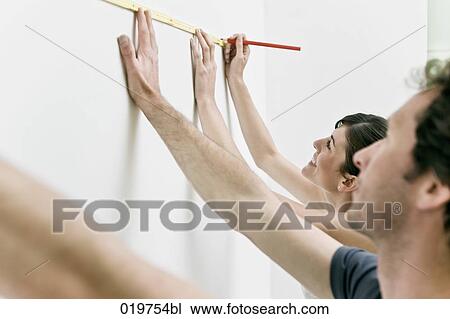Stock Image - young couple making marking on the wall with folding rule and pencil. Fotosearch