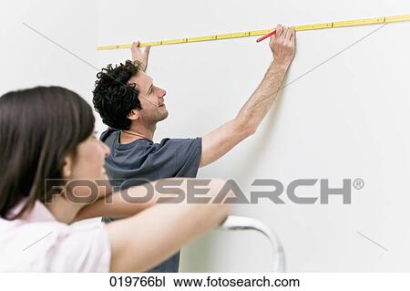 Stock Image - young couple making marking on the wall with folding rule and pencil. Fotosearch