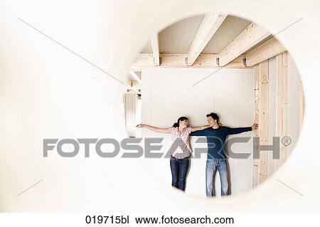 Stock Image - young couple on construction site of their new home seen through hole in wall. Fotosearch