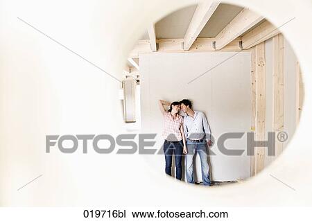 Stock Image - young couple on construction site of their new home seen through hole in wall. Fotosearch