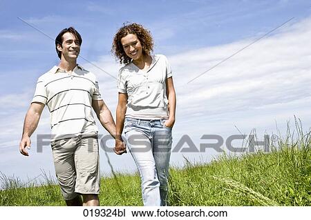 Stock Image - young couple walking hand in hand on meadow. Fotosearch