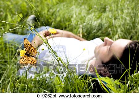Stock Image - young man dozing in grass focus on orange butterfly. Fotosearch