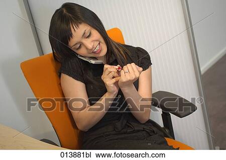 Stock Image - young office worker checking her fingernails while talking on the cellphone. Fotosearch