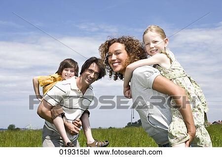 Stock Image - young parents giving their children piggyback ride. Fotosearch