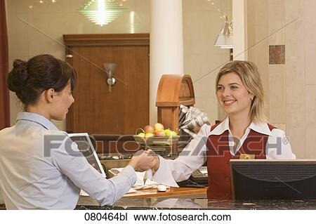 Stock Image - young receptionist handing out key card to female hotel guest. Fotosearch