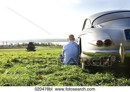 bald man sitting on meadow by his classic car watching landscape View Large Photo Image Stock Image - bald man sitting on meadow by his classic car watching landscape. Fotosearch