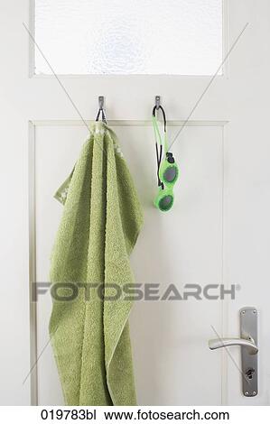 Stock Image - green towel and swimming goggles hanging on bathroom door. Fotosearch