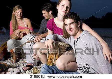 Stock Image - group of friends enjoying beer and sausages on riverbank in summer. Fotosearch
