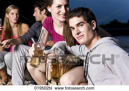 Stock Image - group of friends enjoying beer and sausages on riverbank in summer. Fotosearch