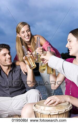 Stock Image - group of friends enjoying some beers at party on riverbank in summer. Fotosearch