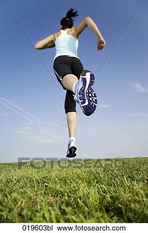 Stock Image - low angle view of young woman jogging through park. Fotosearch