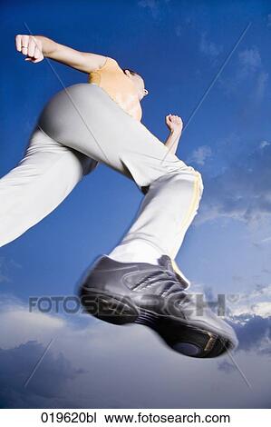 Stock Image - low angle view of young woman jogging through park. Fotosearch