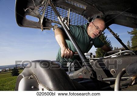 Stock Image - man repairing the engine of his classic car. Fotosearch