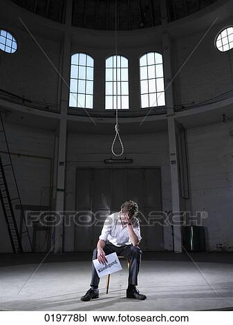 Stock Image - man sitting under rope in empty building holding document with german word for resignation. Fotosearch