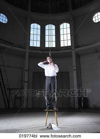 Stock Image - man standing on chair in empty building ready to hang himself. Fotosearch