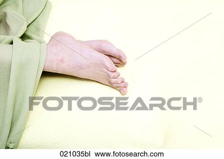 Stock Image - pair of feet sticking out of bedcover. Fotosearch