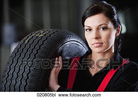 Stock Image - portrait of female mechanic carrying tire. Fotosearch