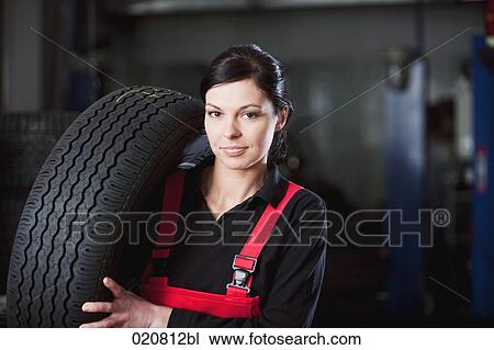 Stock Image - portrait of female mechanic carrying tire. Fotosearch