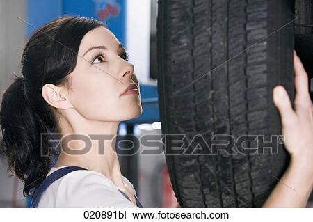 Stock Image - portrait of female mechanic changing tire on car. Fotosearch
