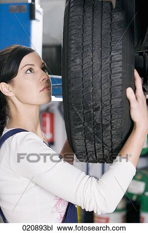 Stock Image - portrait of female mechanic changing tire on car. Fotosearch