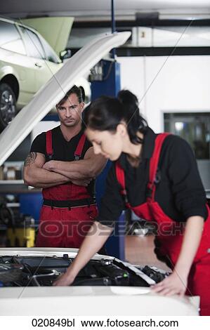 Stock Image - portrait of female mechanic repairing car with male colleague watching. Fotosearch