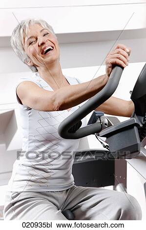 Stock Image - portrait of mature woman on exercise bike at gym. Fotosearch