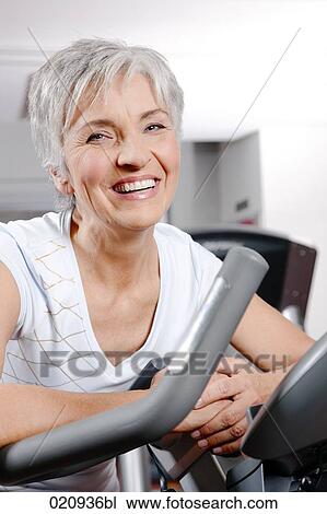 Stock Image - portrait of mature woman on exercise bike at gym. Fotosearch