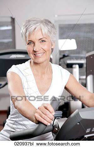 Stock Image - portrait of mature woman on exercise bike at gym. Fotosearch